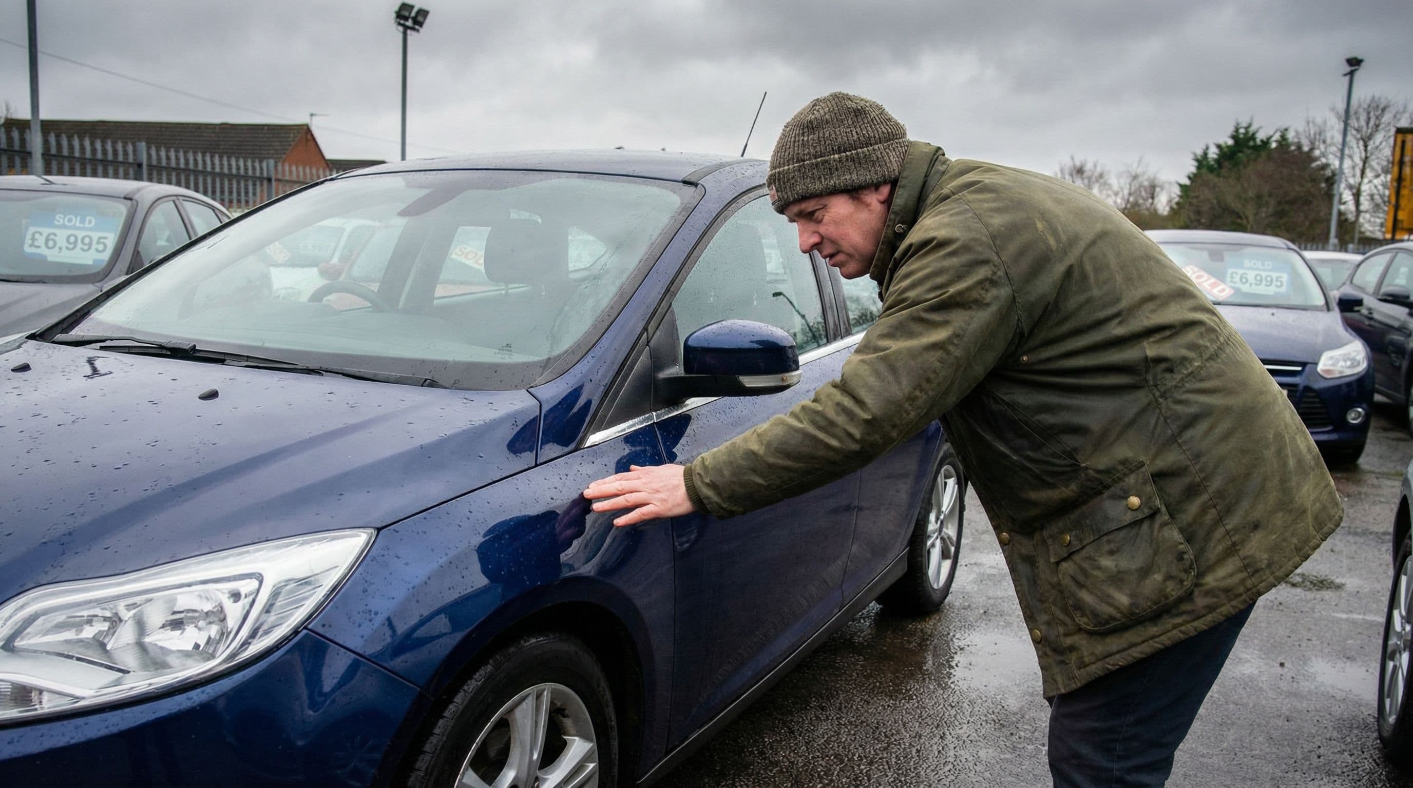 Person carefully examining the paintwork and condition of a used car