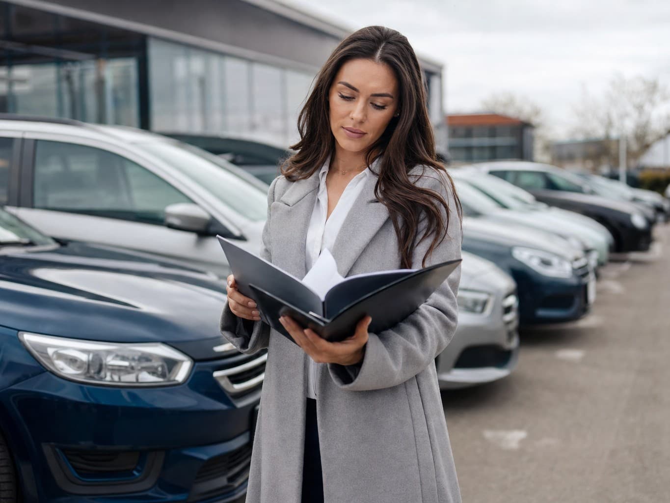 A car buyer reviewing paperwork on a UK dealership forecourt with rows of cars behind