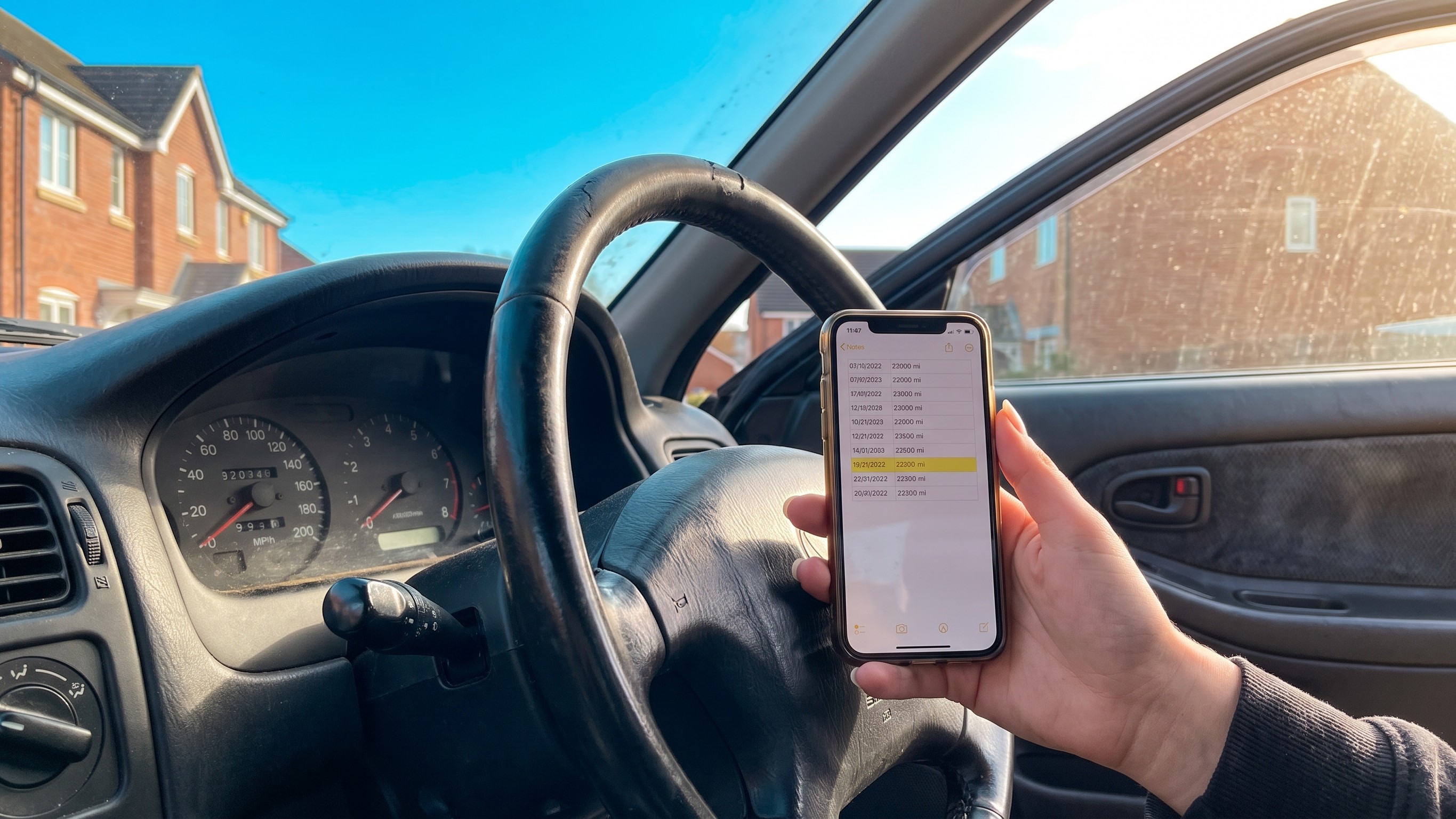The MOT history on a phone, held up beside the car's dashboard