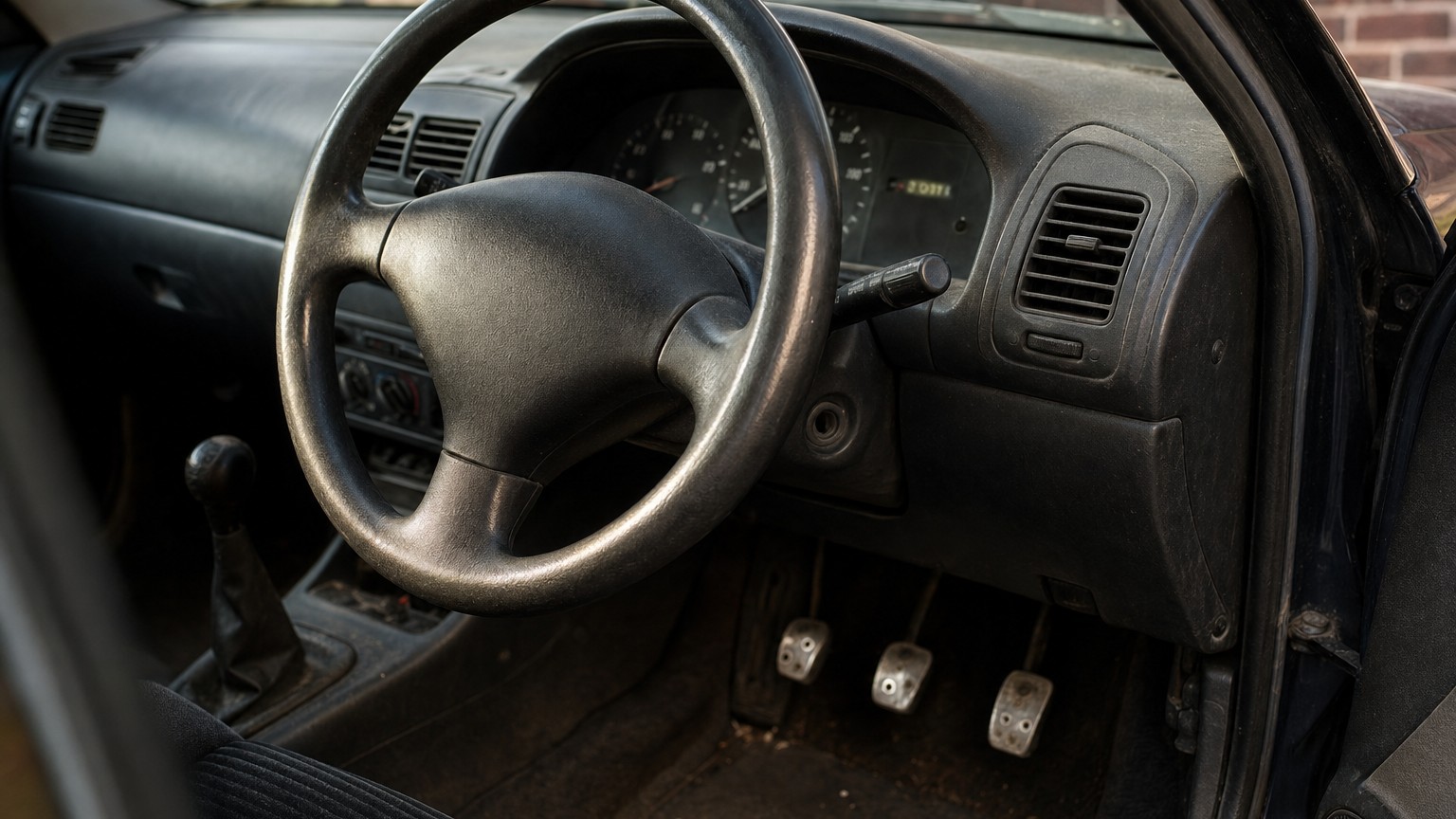 Worn-through pedal rubbers and a steering wheel polished smooth beside a dashboard showing a low mileage